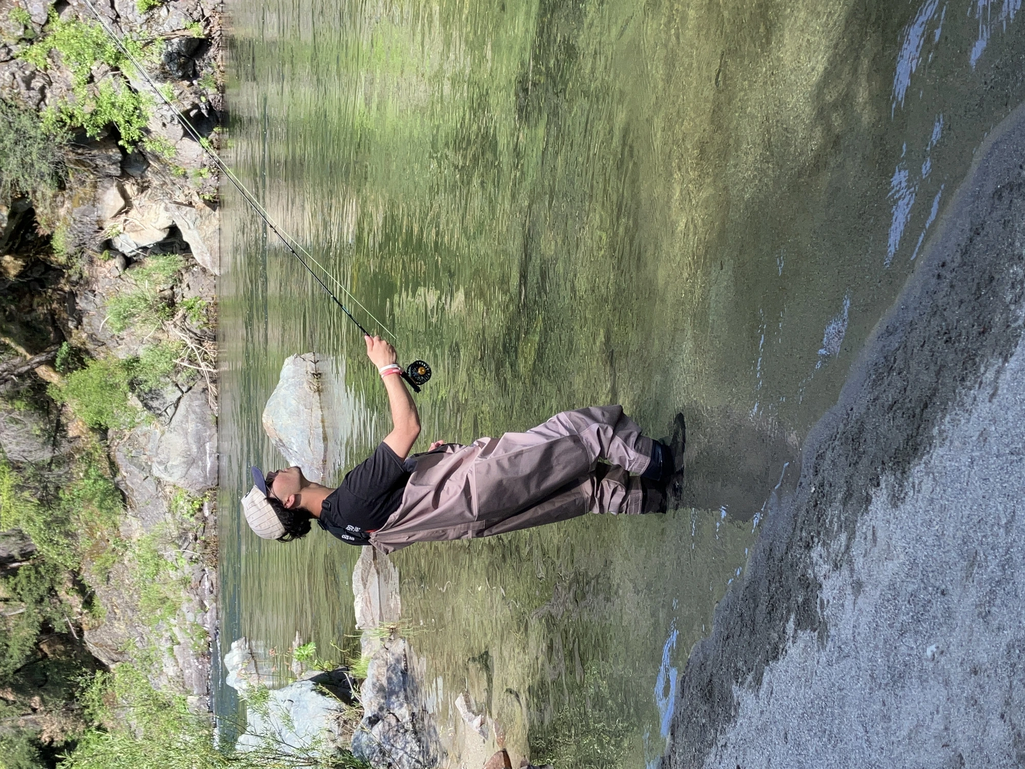 Angler wading a boulder-strewn river with a fly rod