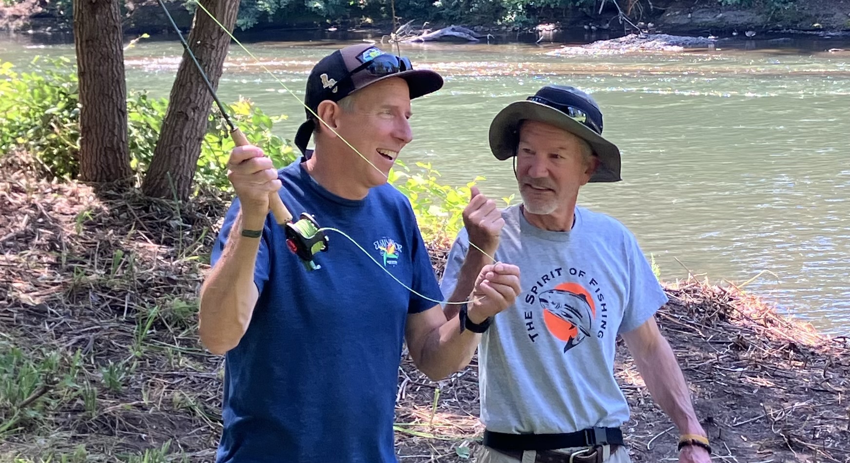 Mike laughing with a student holding a fly rod on the river